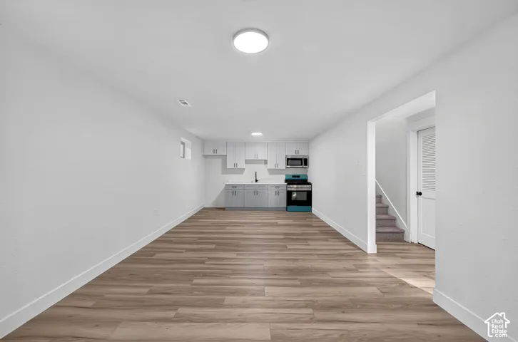 Open-concept kitchen and dining area featuring wood-finish flooring throughout, recessed ceiling lighting, white cabinetry with integrated appliances, and direct access to additional living spaces via interior doorways