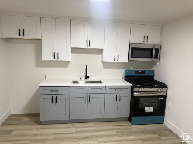 Two-tone cabinetry with ample storage, stainless steel sink with matte black faucet, integrated stainless steel microwave, and wood-finish flooring