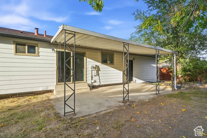 Rear exterior with a covered patio area featuring a concrete pad, metal support columns, and a solid roof