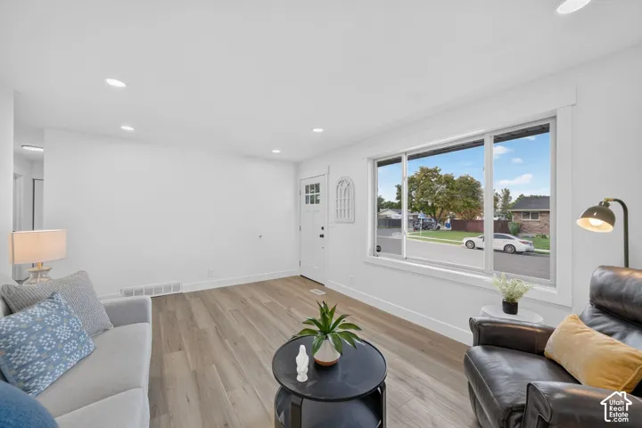Recessed ceiling lighting, wood-finish flooring, white trim, a large window, and a white entry door with glass inserts
