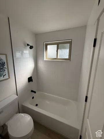 White subway tile shower surround with black fixtures, single glazed window, and wood-finish flooring