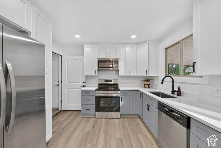 Kitchen featuring two-tone cabinetry, stainless steel appliances, light-toned wood-finish flooring, a matte black faucet, and a large window