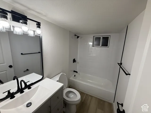 Bathroom featuring a white vanity with integrated sink, black fixtures, wood-finish flooring, and a white subway tile shower surround