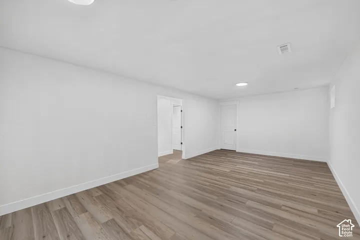Spacious room with wood-finish flooring, white walls, recessed lighting, and a white door with black hardware