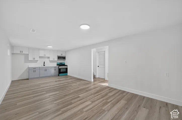 Bright interior with wood-finish flooring, recessed lighting, and a kitchen area featuring white upper cabinetry, gray lower cabinetry, and a black and blue range