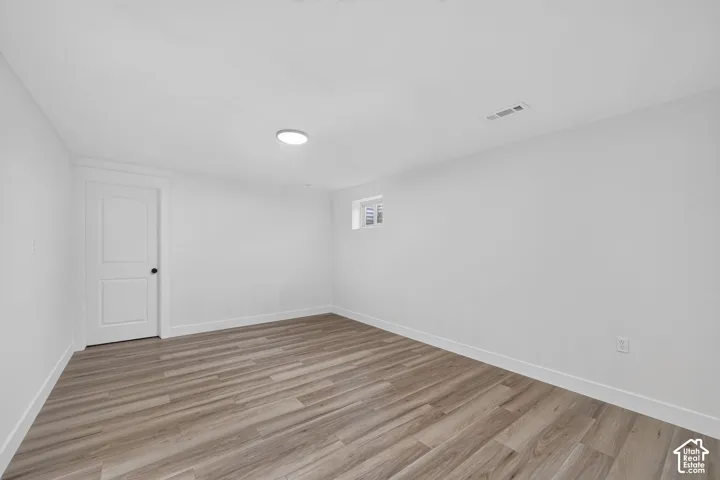 Clean interior with wood-finish flooring, white walls, and a flat-panel door