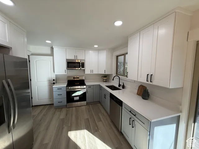 Modern kitchen featuring two-tone cabinetry, stainless steel appliances, a black matte faucet, white countertops, and wood-finish flooring