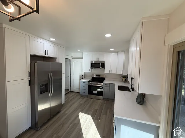 White shaker-style cabinetry with matte black hardware, stainless steel appliances, light-toned wood-finish flooring, recessed lighting, and white countertops