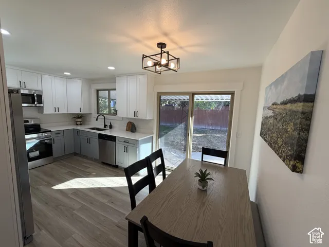 Modern kitchen featuring white and gray cabinetry, stainless steel appliances, wood-finish flooring, and a sliding glass door