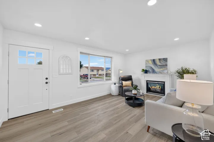 Recessed lighting, wood-finish flooring, white fireplace with hearth, and a front entry door with integrated window panels