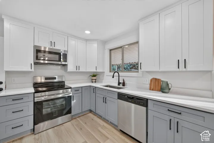 Kitchen featuring two-tone cabinetry, stainless steel appliances, light-toned countertops, wood-finish flooring, and a large window