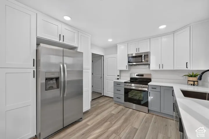 White shaker cabinetry, stainless steel appliances, wood-finish flooring, white countertops, and a stainless steel sink with a black faucet