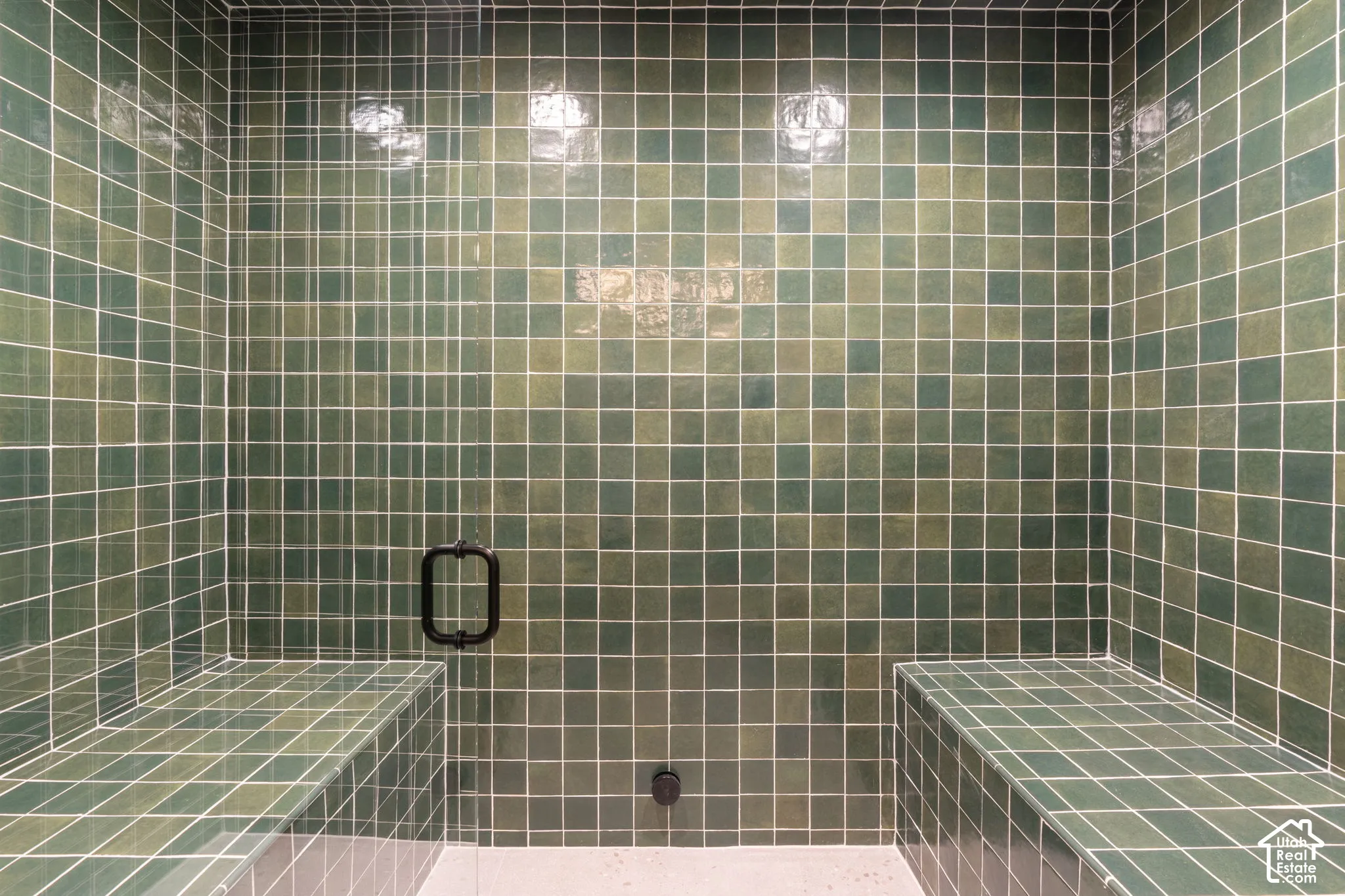 Tiled shower with integrated bench seating, square wall tiling, and a matte black shower door handle