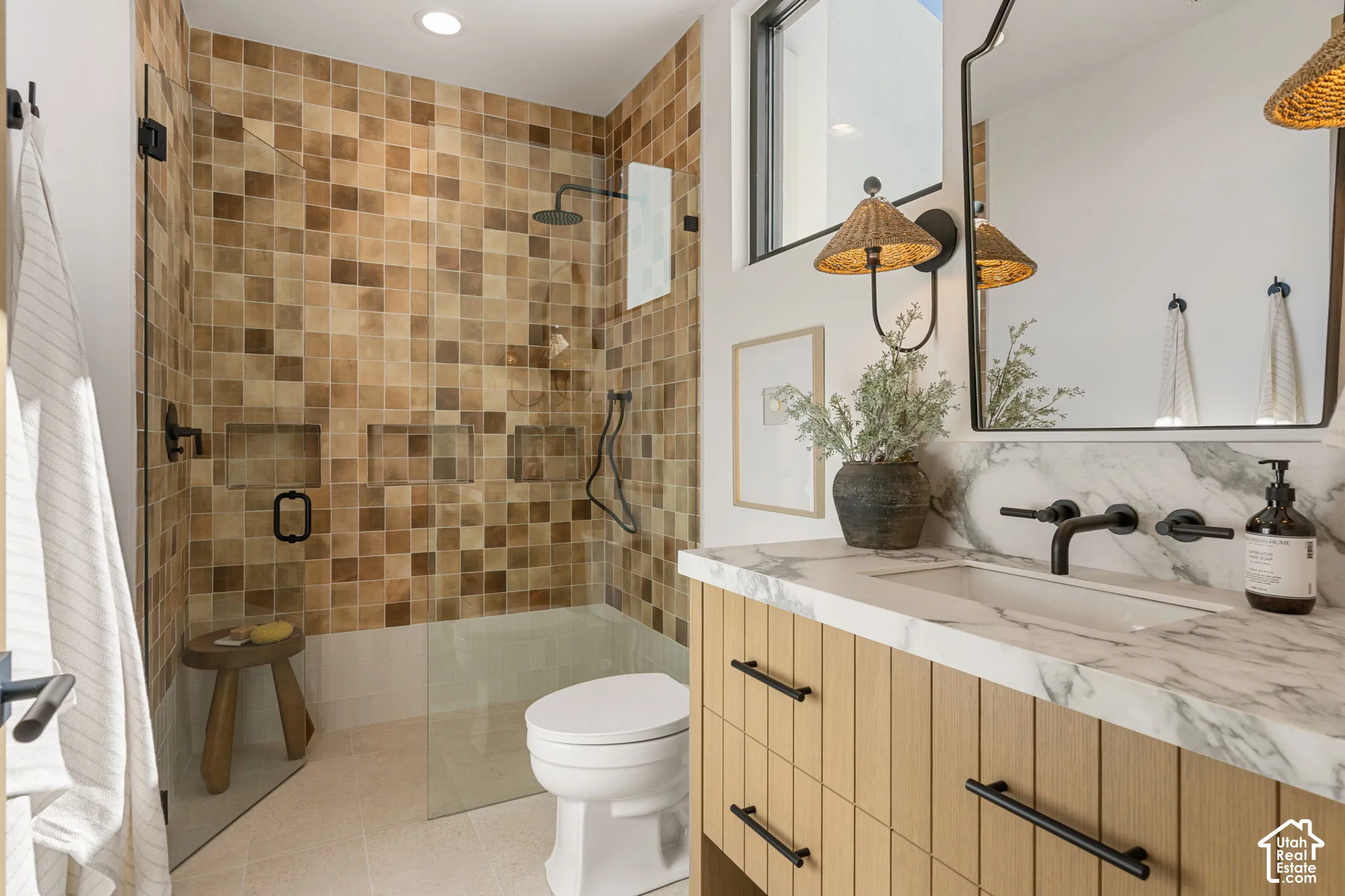 Tiled shower enclosure with built-in niches, glass shower panel, floating vanity with integrated sink, stone countertop, and wall-mounted faucet