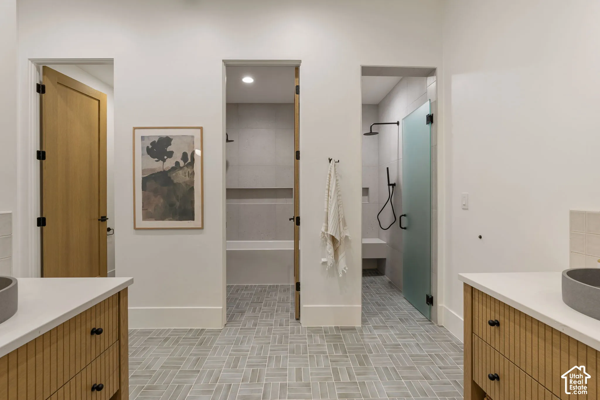 Herringbone tile flooring, dual wood-finish vanities with countertop sinks, and two separate shower enclosures