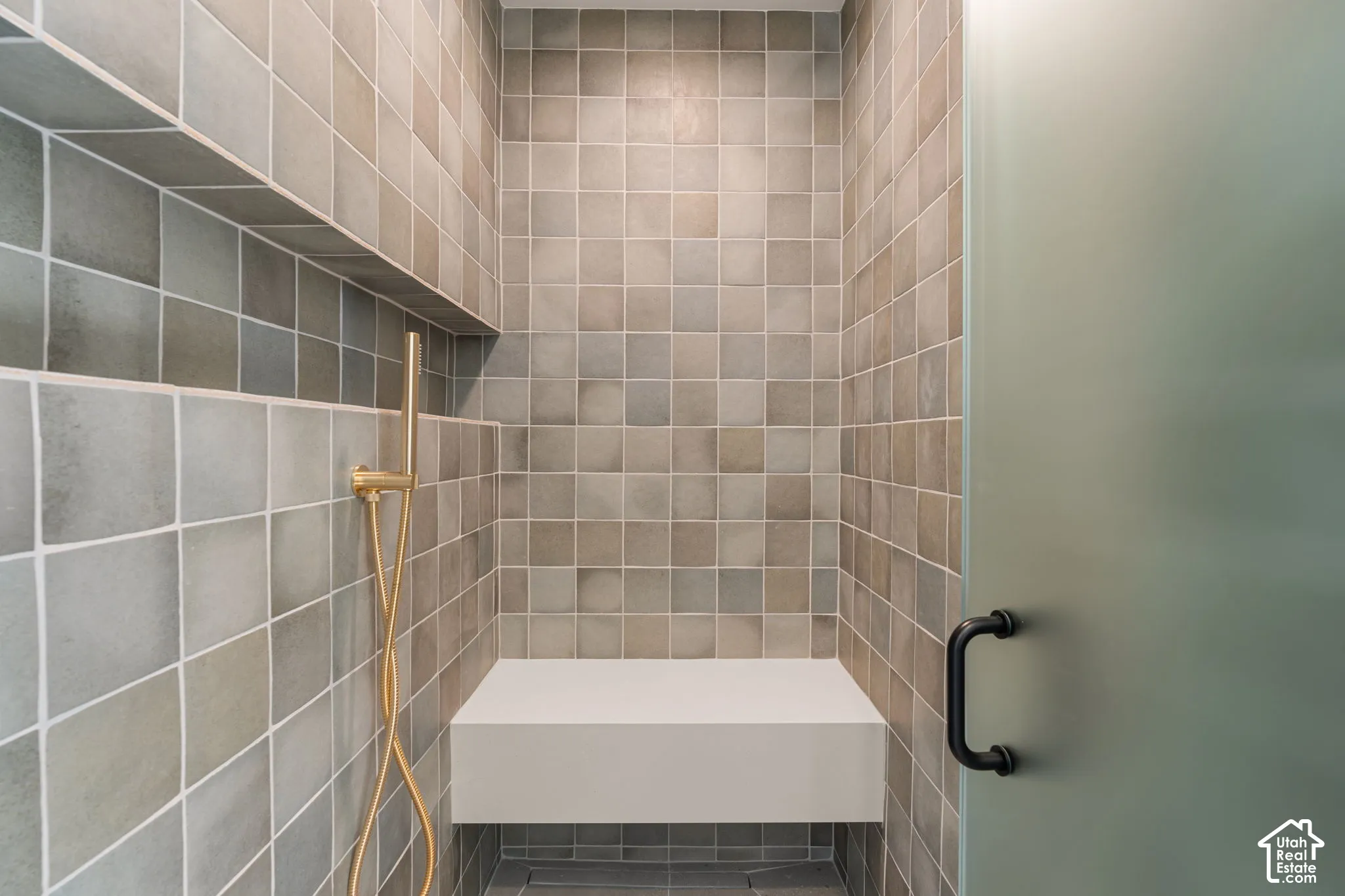 Tiled shower enclosure featuring a built-in bench, recessed shelf, handheld shower fixture, and frosted glass door with a dark-finish handle