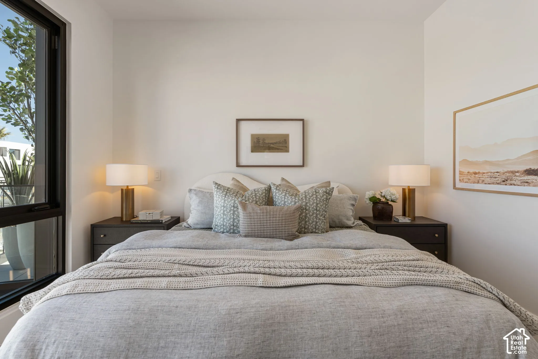 Bright bedroom featuring a large black-framed window, a curved headboard, and two dark wood-finish nightstands with table lamps