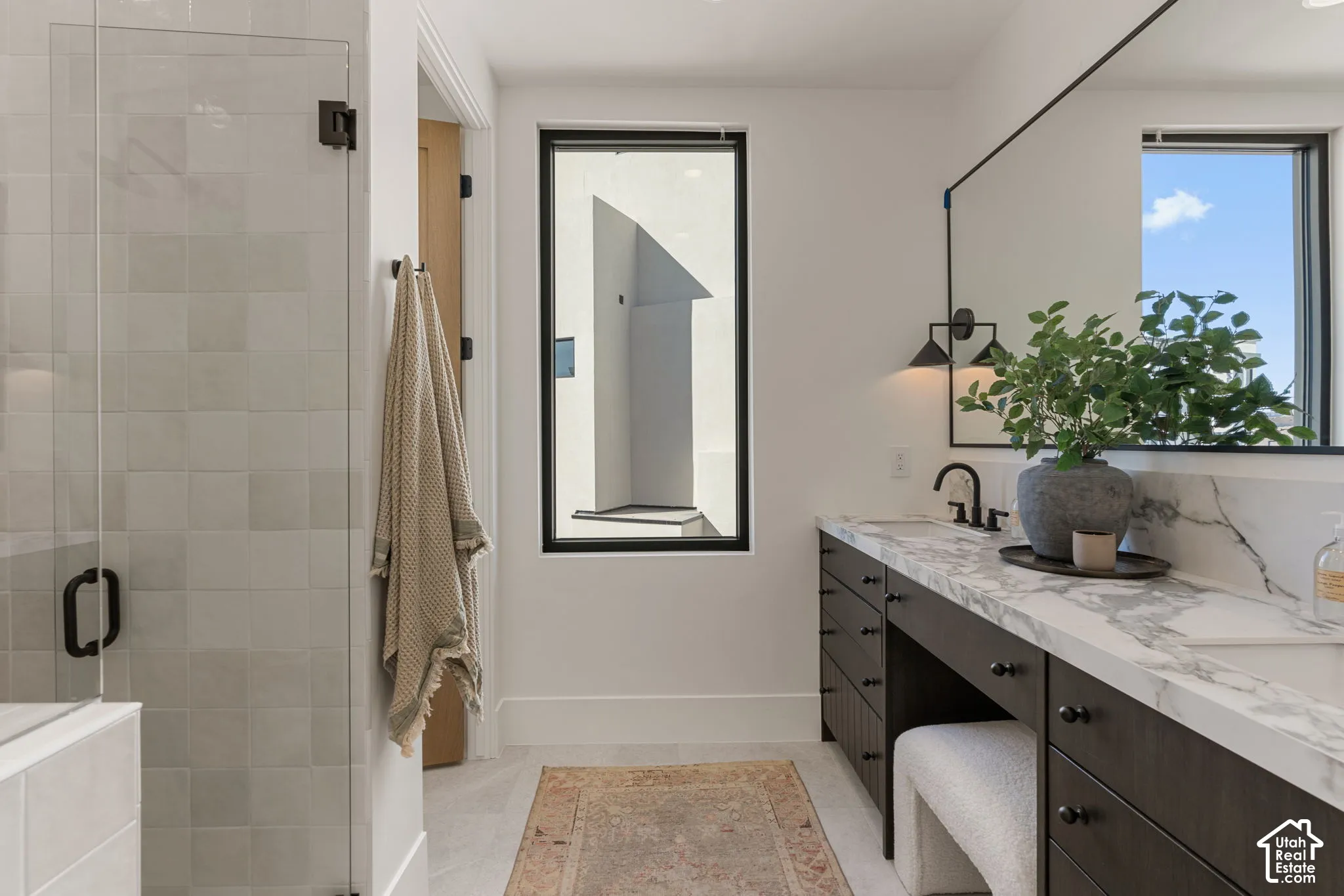 Glass-enclosed shower with tiled walls, dual vanity with stone-finish countertop, dark wood-finish cabinetry, and contemporary black-framed mirror
