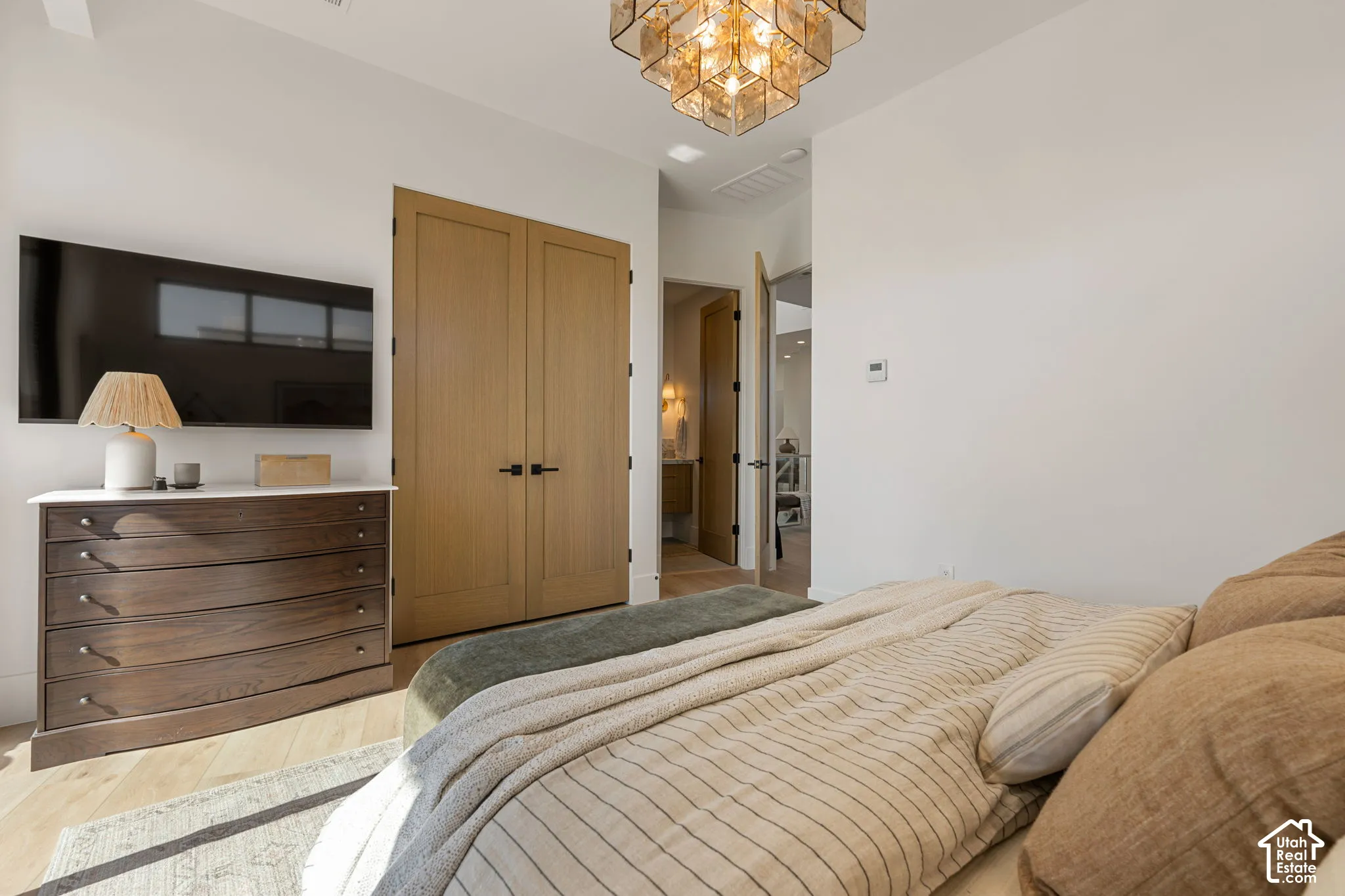 Light wood-finish flooring, two solid wood doors with black hardware, and a modern chandelier
