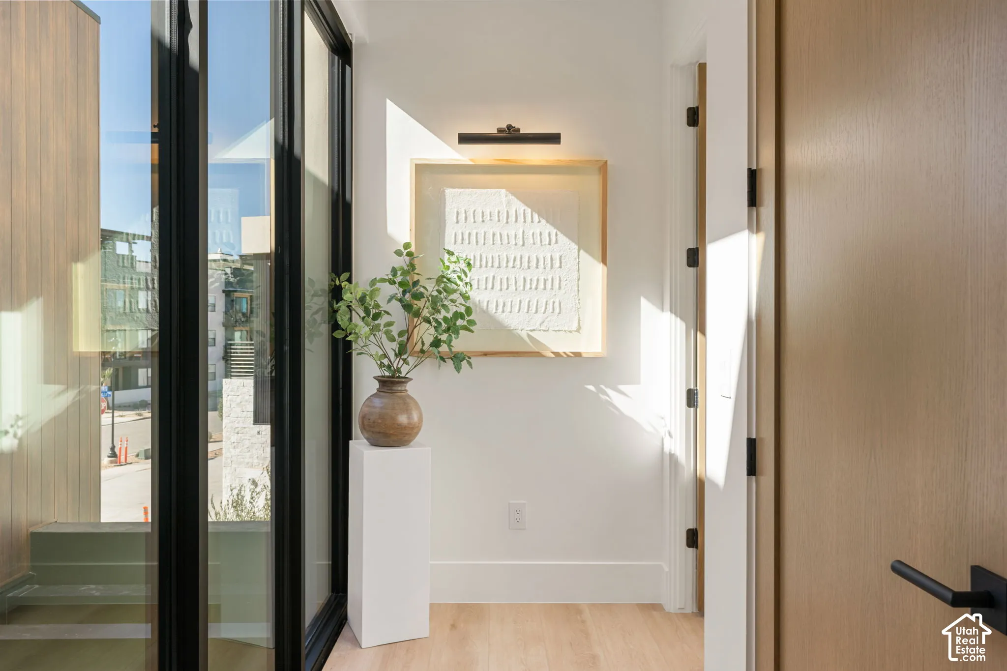 Wood-finish flooring, a light wood-paneled door with matte black hardware, and large black-framed windows