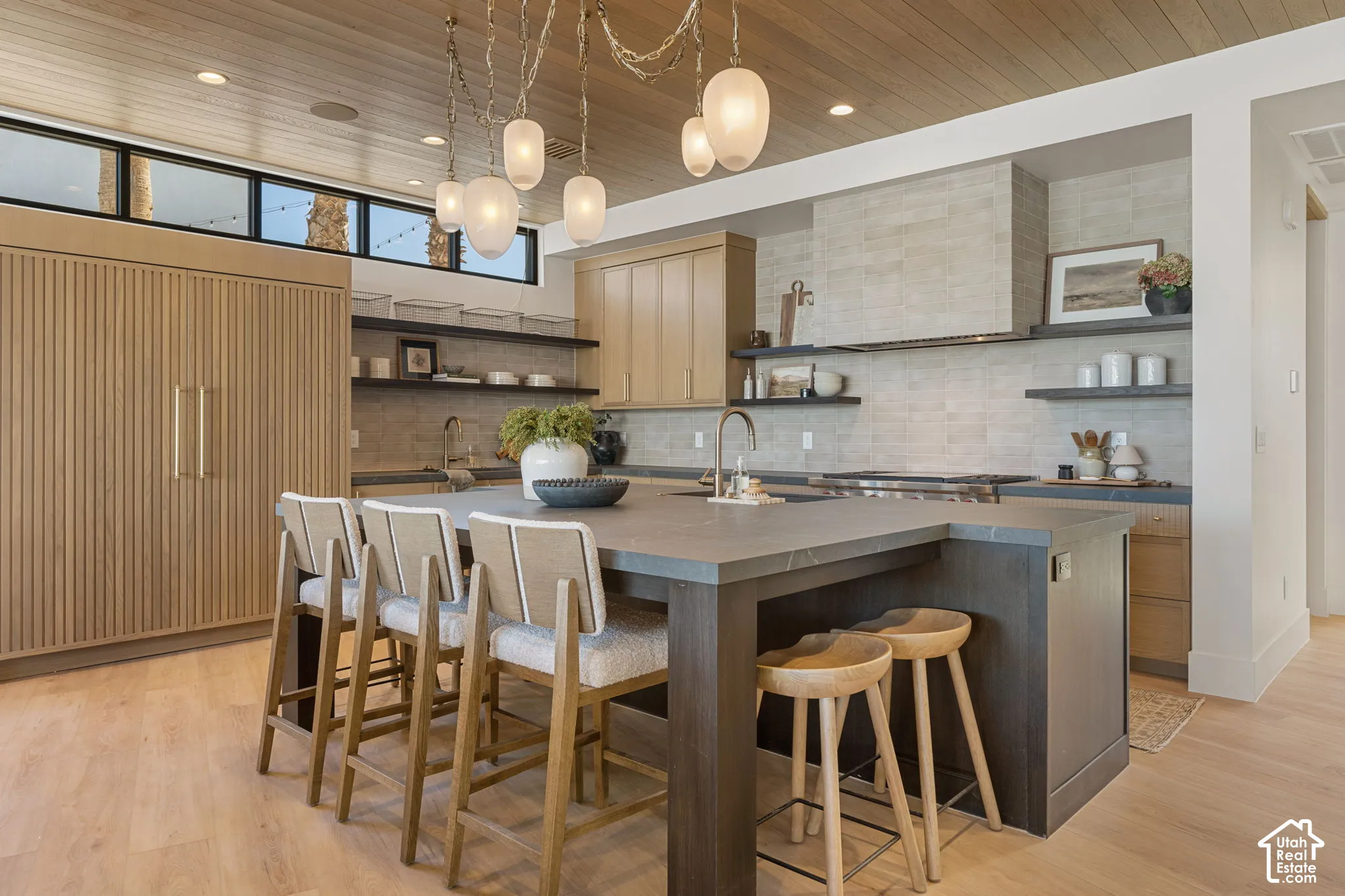 Kitchen featuring a wood-panel ceiling, light wood-finish flooring, a large island with countertop seating, and integrated appliances