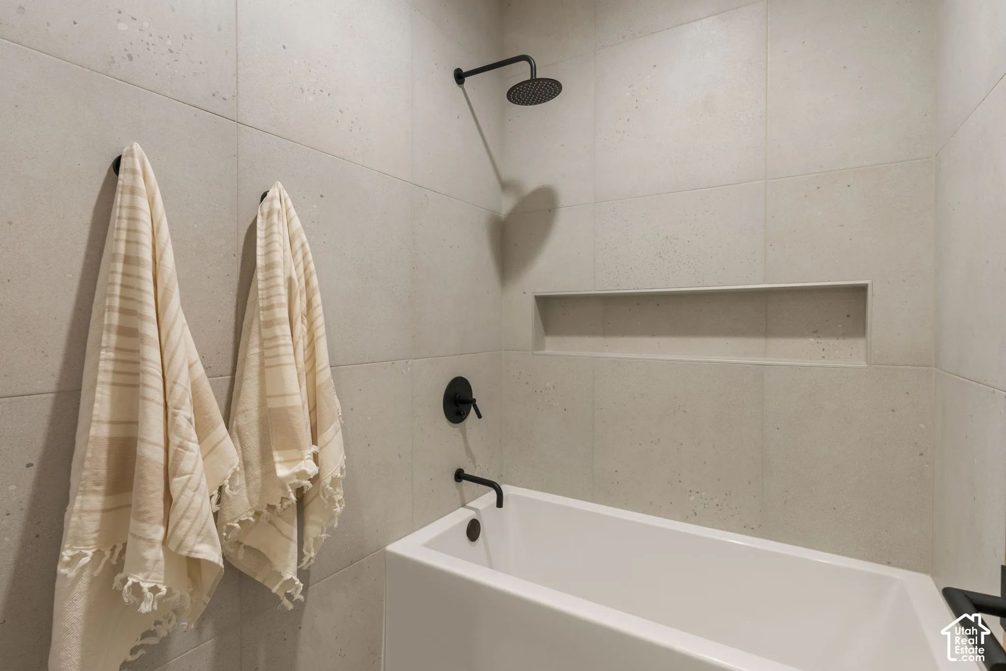 Built-in bathtub with matte black fixtures, integrated shower head, recessed wall niche, and large format wall tiles