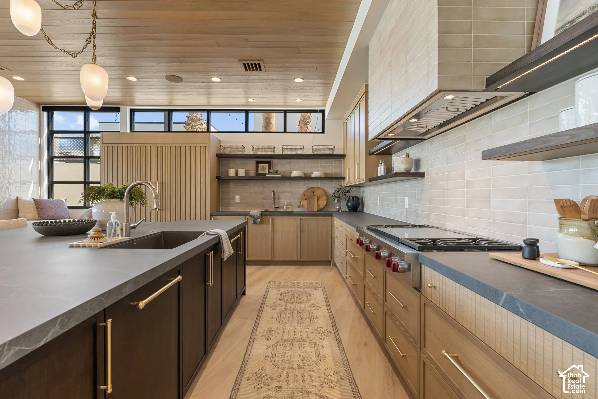 Kitchen featuring a large central island with an undermount sink, a professional-grade range, a tile backsplash, and wood-finish flooring