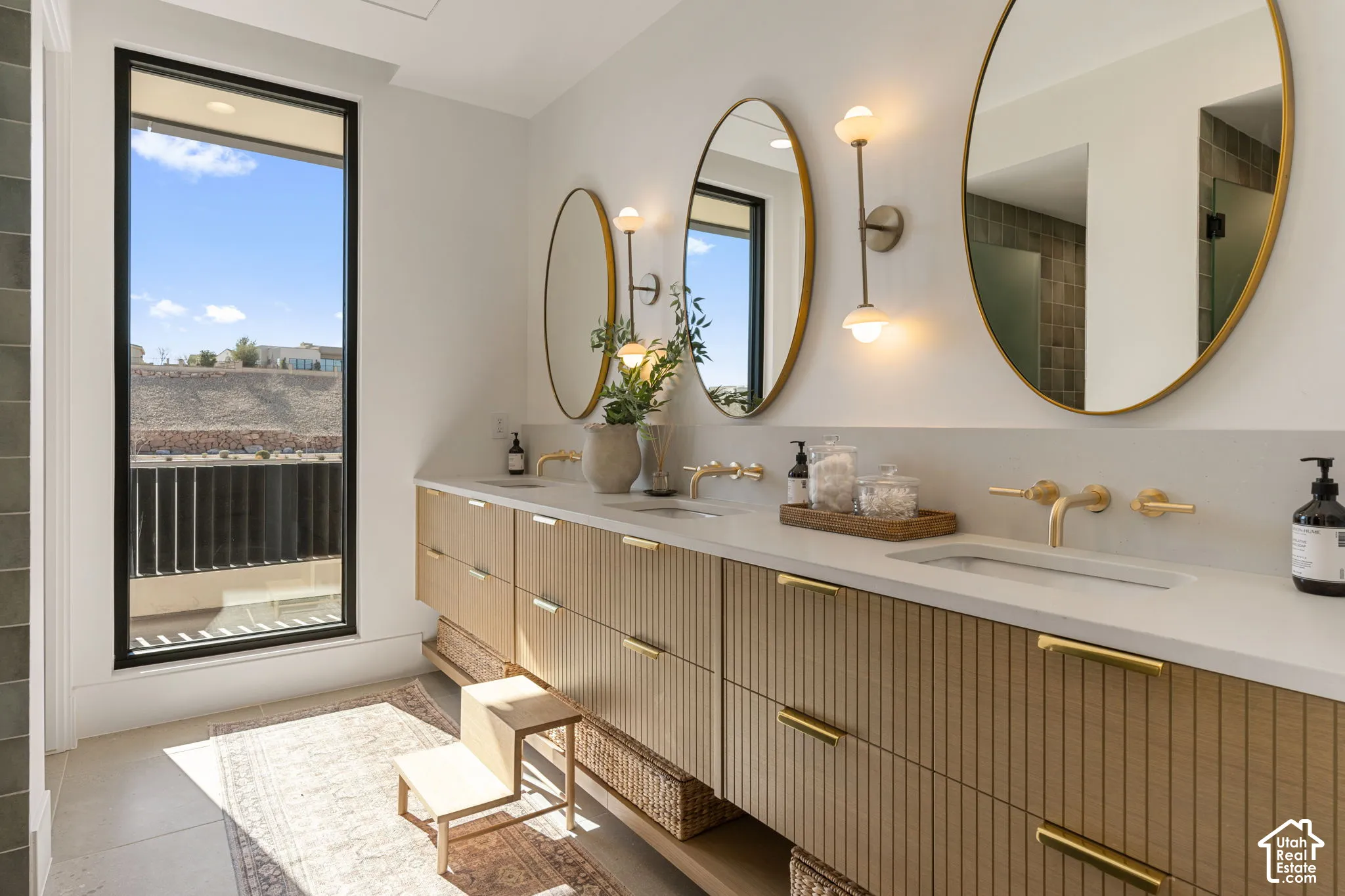 Dual vanity with integrated sinks, wall-mounted gold-finish faucets, and oval mirrors