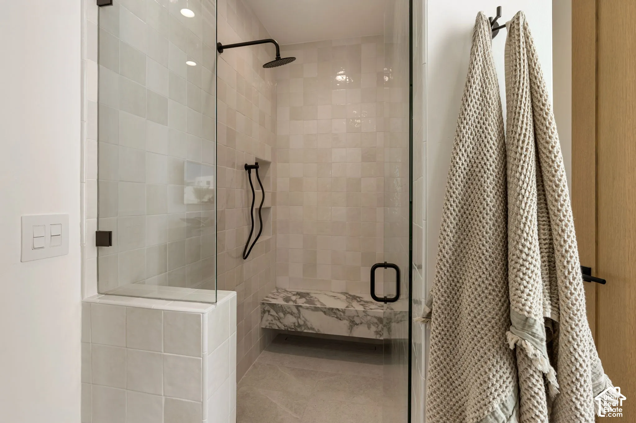 Glass-enclosed shower with matte black fixtures, integrated marble bench, and tiled walls