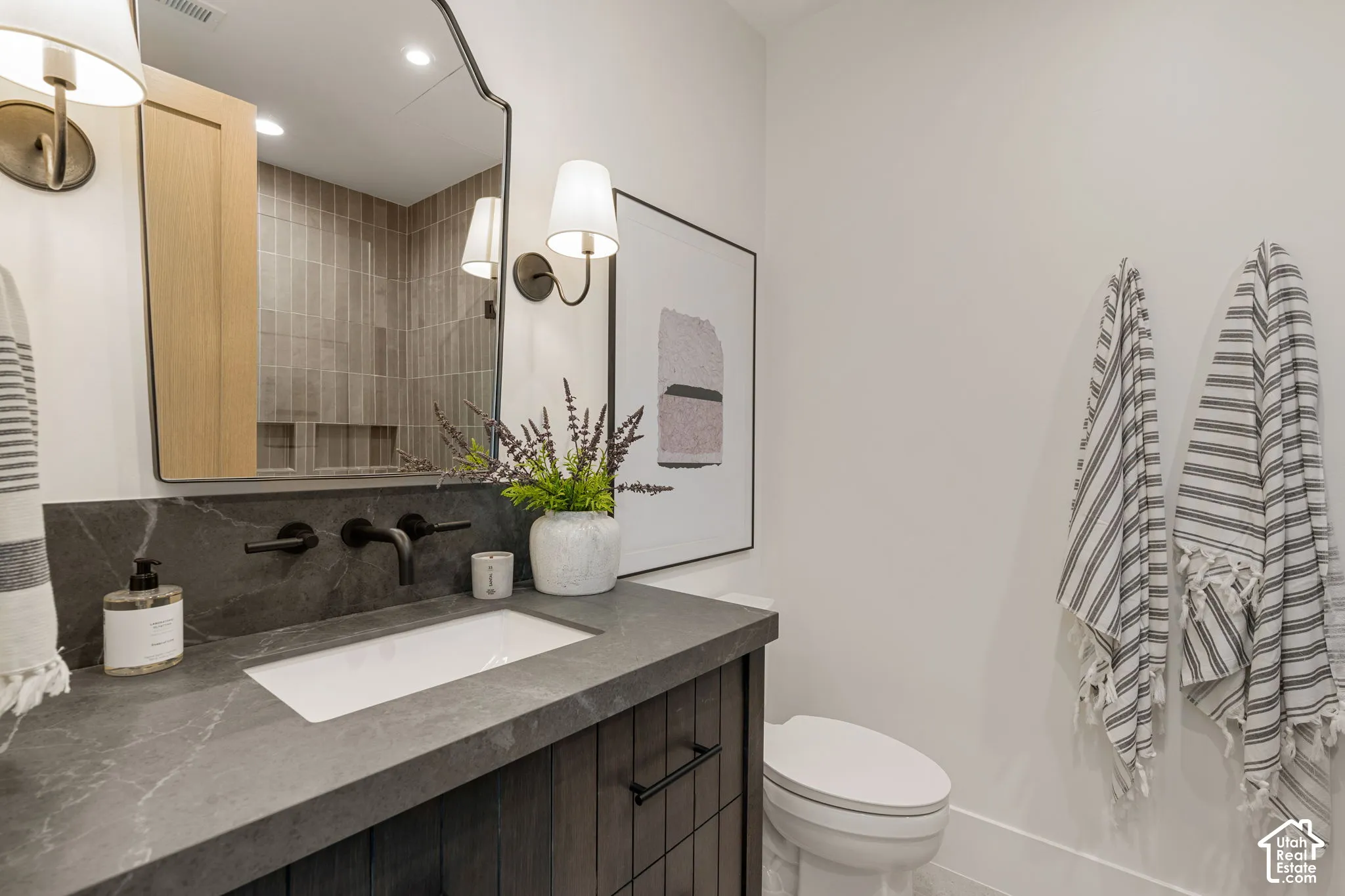 Vanity with an integrated rectangular sink, wall-mounted matte black faucet, and dark stone countertop
