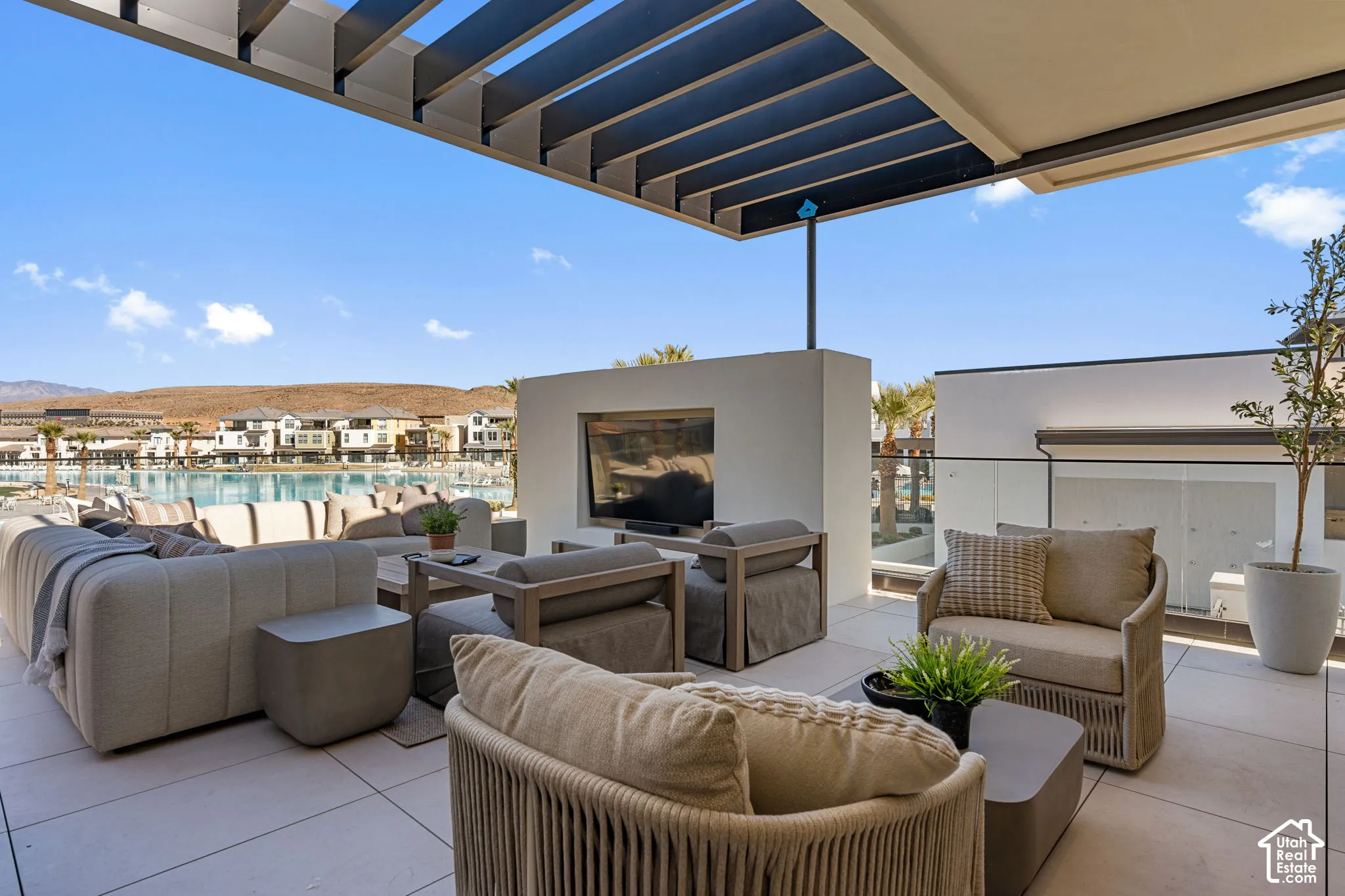Expansive outdoor patio featuring a slatted pergola, built-in media center, tile flooring, and glass railing