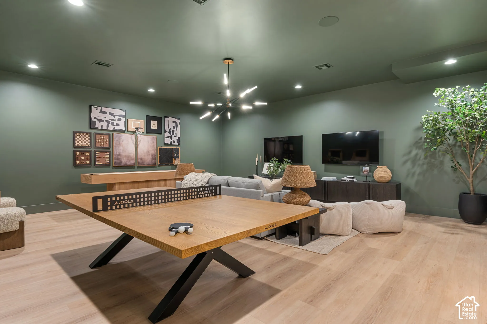 Spacious recreational room with light wood-finish flooring, recessed lighting, and a modern chandelier