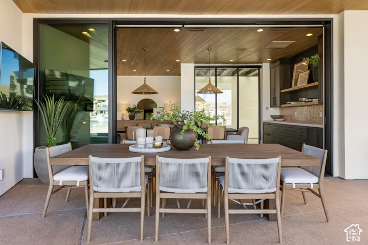 Outdoor dining area featuring a wood-finish dining table, a wood-paneled ceiling, recessed lighting, and large sliding glass doors