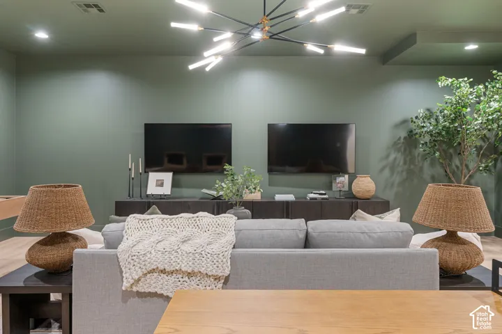 Recessed lighting, modern linear chandelier, wood-finish flooring, two wall-mounted flat-panel screens, built-in media console