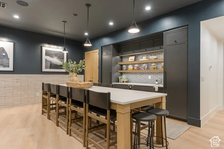 Expansive island with a light-toned countertop, wood-finish flooring, built-in cabinetry, hexagon tile backsplash, and pendant lighting
