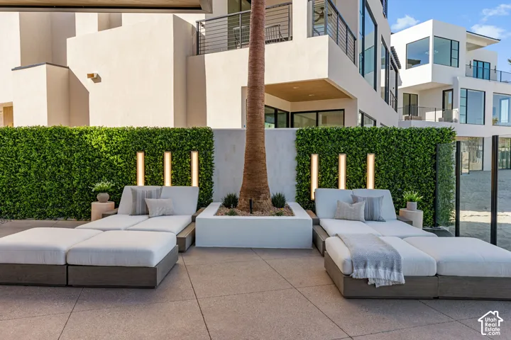 Paved outdoor patio area with a privacy hedge, three vertical wall lights, and a palm tree in a planter