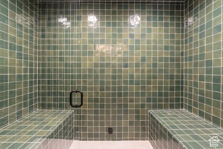 Tiled shower with integrated bench seating, square wall tiling, and a matte black shower door handle