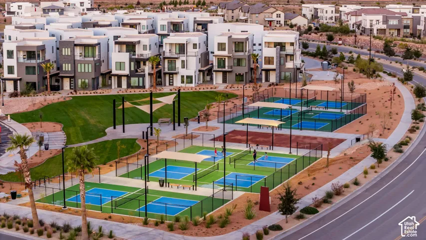 Modern multi-story residences surround a community park with a large grass area, multiple pickleball courts, and paved walkways