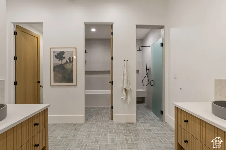 Herringbone tile flooring, dual wood-finish vanities with countertop sinks, and two separate shower enclosures