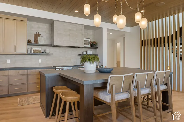 Open-concept kitchen with wood-finish flooring, a large center island, extensive cabinetry, tile backsplash, and a wood slat accent wall