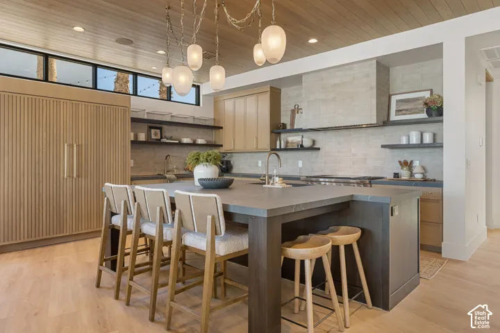 Kitchen featuring a wood-panel ceiling, light wood-finish flooring, a large island with countertop seating, and integrated appliances