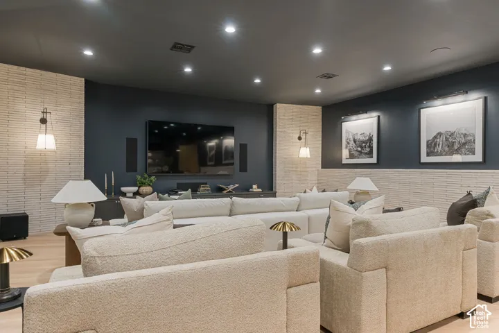 Recessed ceiling lighting, wood-finish flooring, accent wall with linear brick pattern, built-in display console, and wall-mounted sconces