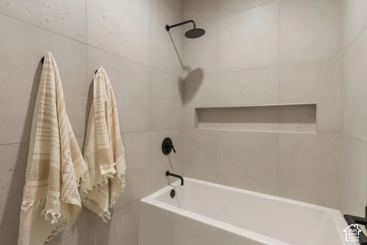 Built-in bathtub with matte black fixtures, integrated shower head, recessed wall niche, and large format wall tiles