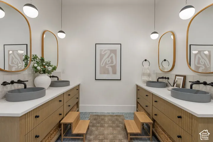 Dual wood-finish vanities with fluted detailing, twin vessel sinks, wall-mounted matte black faucets, and oval mirrors