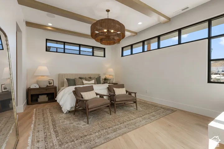 Light wood-finish flooring, exposed ceiling beams, a decorative chandelier, and black-framed windows