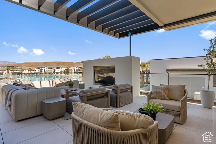 Expansive outdoor patio featuring a slatted pergola, built-in media center, tile flooring, and glass railing