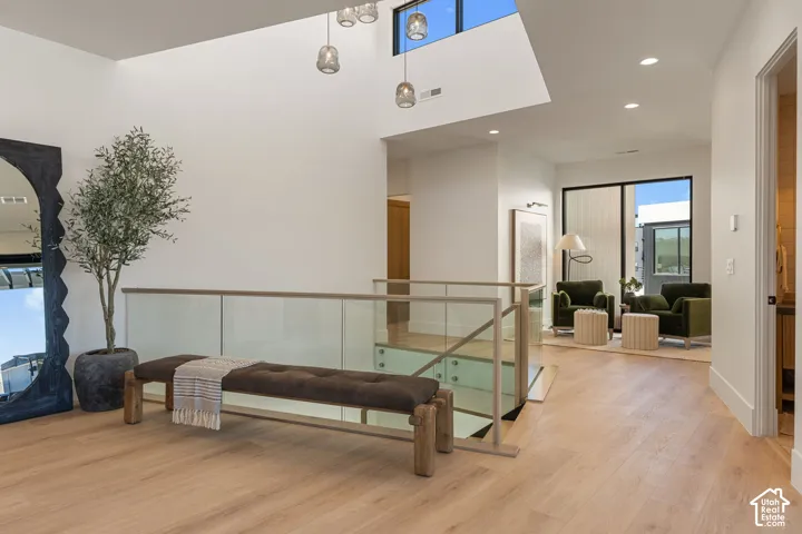Expansive upper landing featuring light wood-finish flooring, a glass railing, abundant natural light from skylights, and recessed lighting