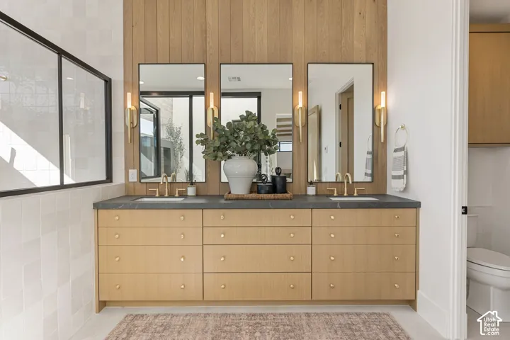 Dual vanity with light wood-finish cabinetry, black countertops, and brushed gold fixtures