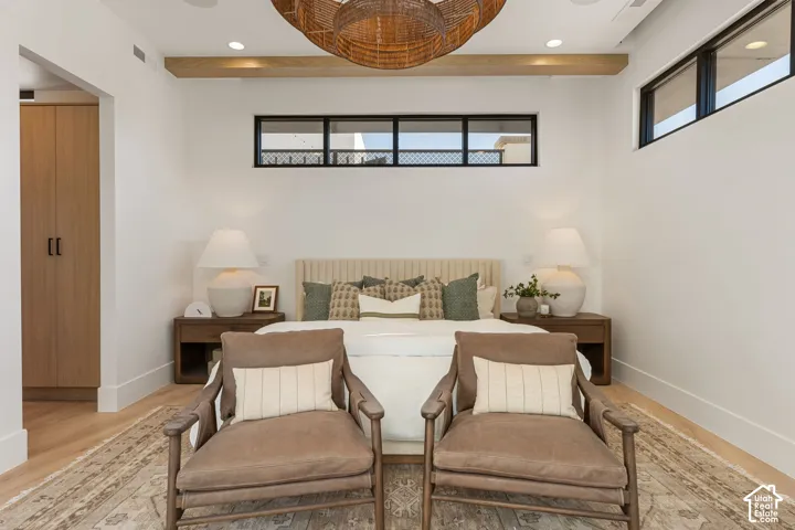 Bedroom featuring light wood-finish flooring, high ceilings with exposed wood beams, built-in cabinetry, and transom windows