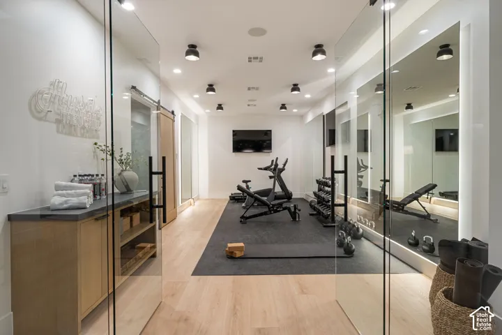 Glass sliding doors open to a dedicated fitness area featuring wood-finish flooring, recessed lighting, and mirrored walls
